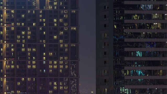 Tall blocks of flats with many glowing windows located in residential district of city aerial timelapse. Evening light in rooms in big towers and skyscrapers