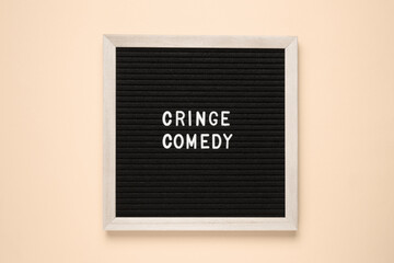 A black rectangle wooden sign with cringe comedy written in a bold font. The pattern and graphics of the logo stand out in the room