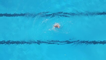 A female athlete performs synchronized swimming routines in an outdoor pool, as seen from the air