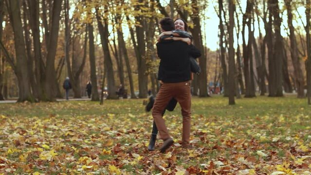 Young loving couple outside in the city park sunny weather, whirl hugging, man holds woman in his arms, orange yellow red maple leaves, hugging smiling kissing laughing spending time together. Autumn