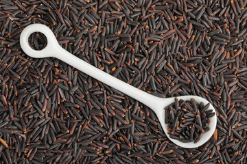 Black rice in a ceramic spoon as a background. Top view. Flat lay
