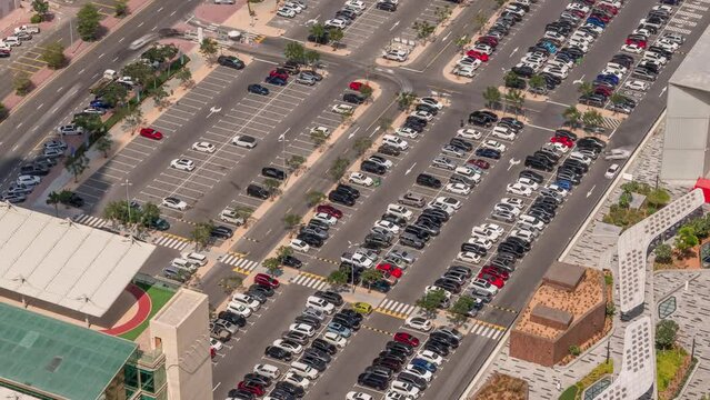 Aerial view of many colorful cars parked on parking lot with lines and markings for parking places and directions timelapse during all day. Long shadows moving fast. Dubai financial center