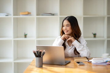 A thoughtful woman engages with her laptop at office, smartphone, and work materials in office.