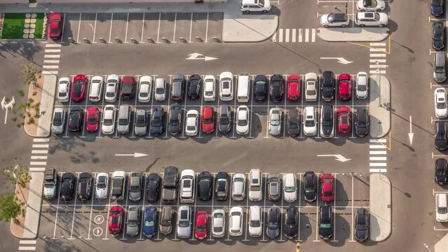 Aerial view of many colorful cars parked on parking lot with lines and markings for places and directions during all day timelapse with long shadows moving fast. Dubai financial district avenue