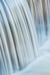 Portage Creek Cascade captured with motion blur and illuminated by reflected color from sunlit trees at sunrise and blue sky overhead, Michigan, USA