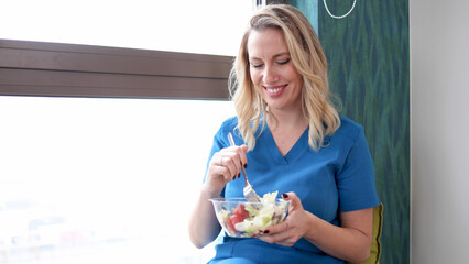 Happy mid adult nurse eating salad and enjoying her lunch break