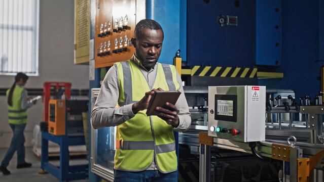 Handsome African American manager wearing vest while working at corporate tablet device. Professional worker entering data from digital gadget to mechanism with touch screen. Business industry. - Powered by Adobe