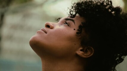 Close-up face of a contemplative black woman gazing upwards at sky, closing and opening eyes in meditative moment