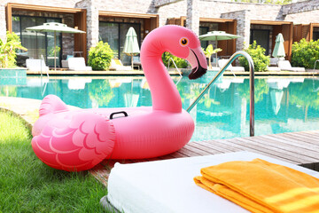 Fototapeta premium Float in shape of flamingo on wooden deck near swimming pool and sunbeds at luxury resort