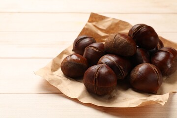 Roasted edible sweet chestnuts on wooden table, space for text
