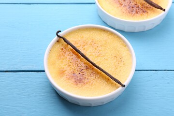 Delicious creme brulee in bowls and vanilla pods on light blue wooden table