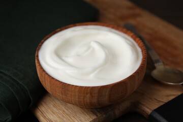 Delicious natural yogurt in bowl and spoon on table, closeup