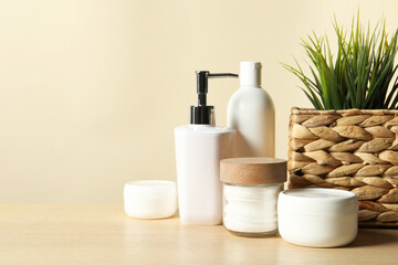 Different bath accessories and houseplant on wooden table against beige background, closeup. Space for text