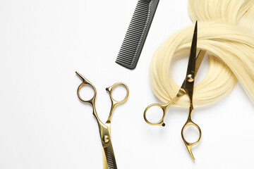 Professional hairdresser scissors and comb with blonde hair strand on white background, flat lay