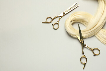 Professional hairdresser scissors with blonde hair strand on light grey background, flat lay. Space...