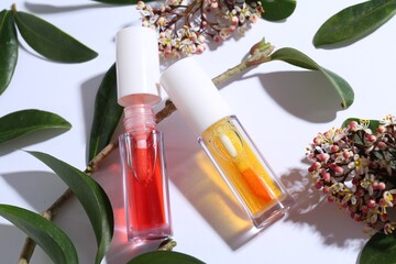 Bright lip glosses, branch, green leaves and flowers on white background, above view