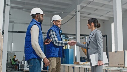 Busy engaged energetic entrepreneur female cooperating discussing with enthusiastic Caucasian man wearing blue vest and white helmet. His thoughtful serious colleague carefully listening.