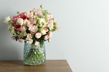Beautiful bouquet of fresh flowers in vase on wooden table near light wall, space for text