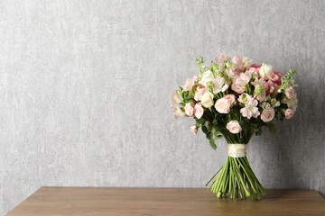Beautiful bouquet of fresh flowers on wooden table near grey wall, space for text