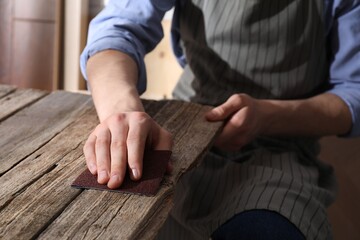 Man polishing wooden table with sandpaper indoors, closeup