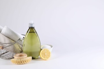 Bottle of cleaning product, brush, rags and lemon on light background