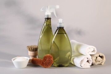 Bottles of cleaning product, brushes, rags and baking soda on light background