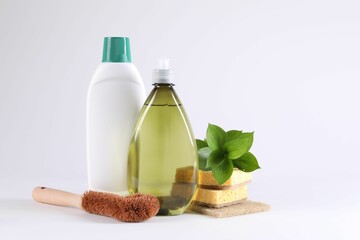 Bottles of cleaning product, brush, sponges and floral decor on white background