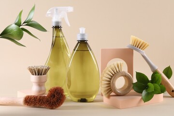 Bottles of cleaning product, brushes and floral decor on beige background