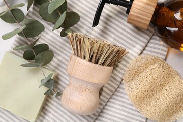 Cleaning brush, sponge, dispenser, soap bar and eucalyptus leaves on table, top view