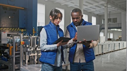 Male African-American worker working talking together with Caucasian female employee. Man counting typing information in his laptop. Woman looking into gadgets. Cooperation concept.