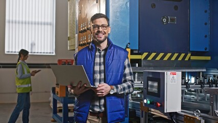 Conscientious good-looking Caucasian bearded male engineer industrial worker wearing glasses look in his modern laptop. Happy joyful man looking in camera smiling chuckling.