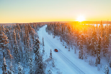 Car travels the icy and empty road crossing the boreal snowy forest at sunrise, Swedish Lapland, Sweden, Scandinavia