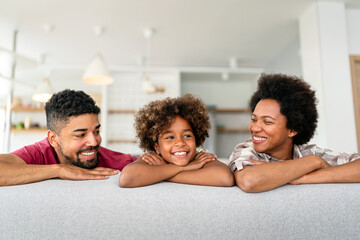 Happy biracial girl smiling with young multiracial parents enjoy weekend at home together, - 780624684
