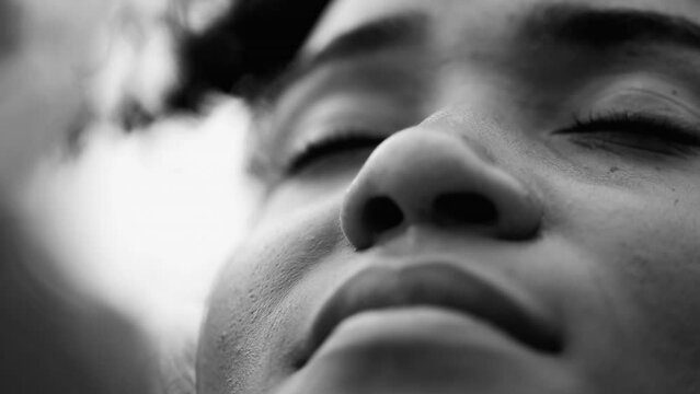 One contemplative young black woman closing eyes in quiet peaceful meditation in artistic black and white, macro close-up of face in silent retreat