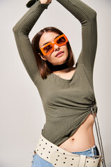 A young woman with brunette hair striking a pose in a green shirt and orange sunglasses.