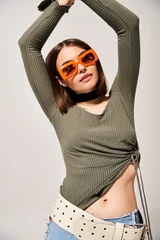  A young woman with brunette hair striking a pose in a green shirt and orange sunglasses. © LIGHTFIELD STUDIOS