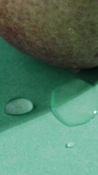 video verticale, primo piano di una pera con gocce d'acqua sulla buccia e sul tavolo, sfondo verde