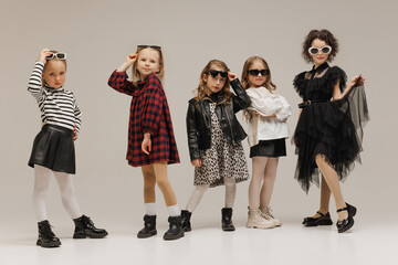 Cool little girls, elementary students posing wearing glamour outfits against grey studio...