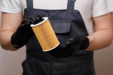 Auto repairman holds and rotates oil filter for diesel cars in black gloves, close-up. Concept of...