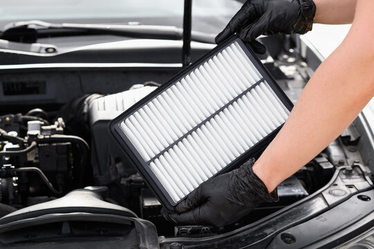 Replacing the air filter in a car. Auto mechanic in gray gloves holds an engine air filter against the engine compartment. Concept of maintenance, ecology, car care, auto parts