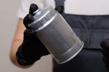 Auto mechanic holds fuel filter for diesel cars in his hands in black gloves, rotating it in his...