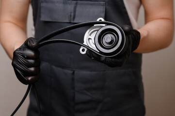 Auto parts salesman holds a tension pulley and a serpentine belt in his hands. Timely replacement...