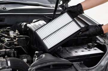Car mechanic holds car air filter in hands near engine compartment, plans to replace old filter,...