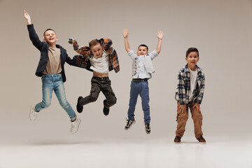 Cute, cool attitude little boys, elementary students jumping of joy and happiness against grey...