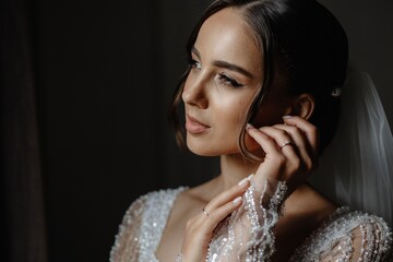 Elegant bride with dark hair and lace wedding dress adjusting her earring