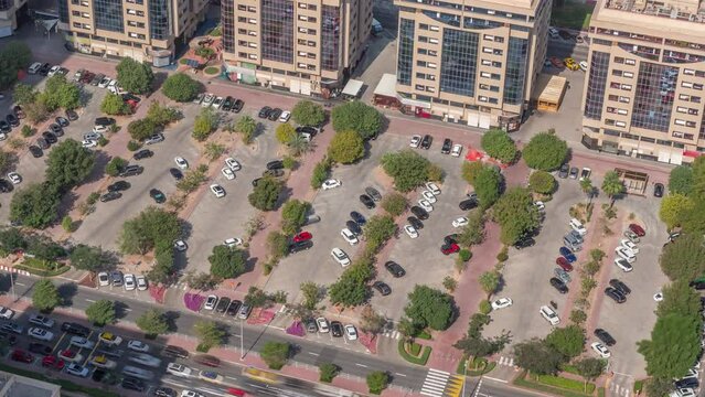 Aerial view of colorful cars parked on parking lot with lines and markings for places and directions timelapse during all day. Green trees around. Financial district in Dubai. Long shadows moving fast