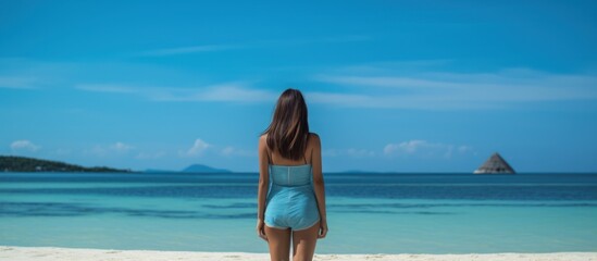 back view of Asian woman in bikini with view of white sandy beach Turquoise water