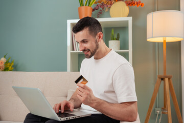 Young man shopping online, holding a credit card and using a laptop computer.