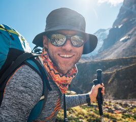 Portrait Young hiker backpacker man in sunglasses smiling at camera in Makalu Barun Park route during high altitude acclimatization walk. Mera peak trekking route, Nepal. Active vacation concept image
