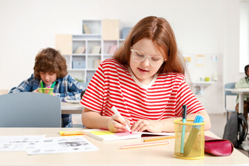Teenage girl sitting at desk in classroom and writing during lesson at school